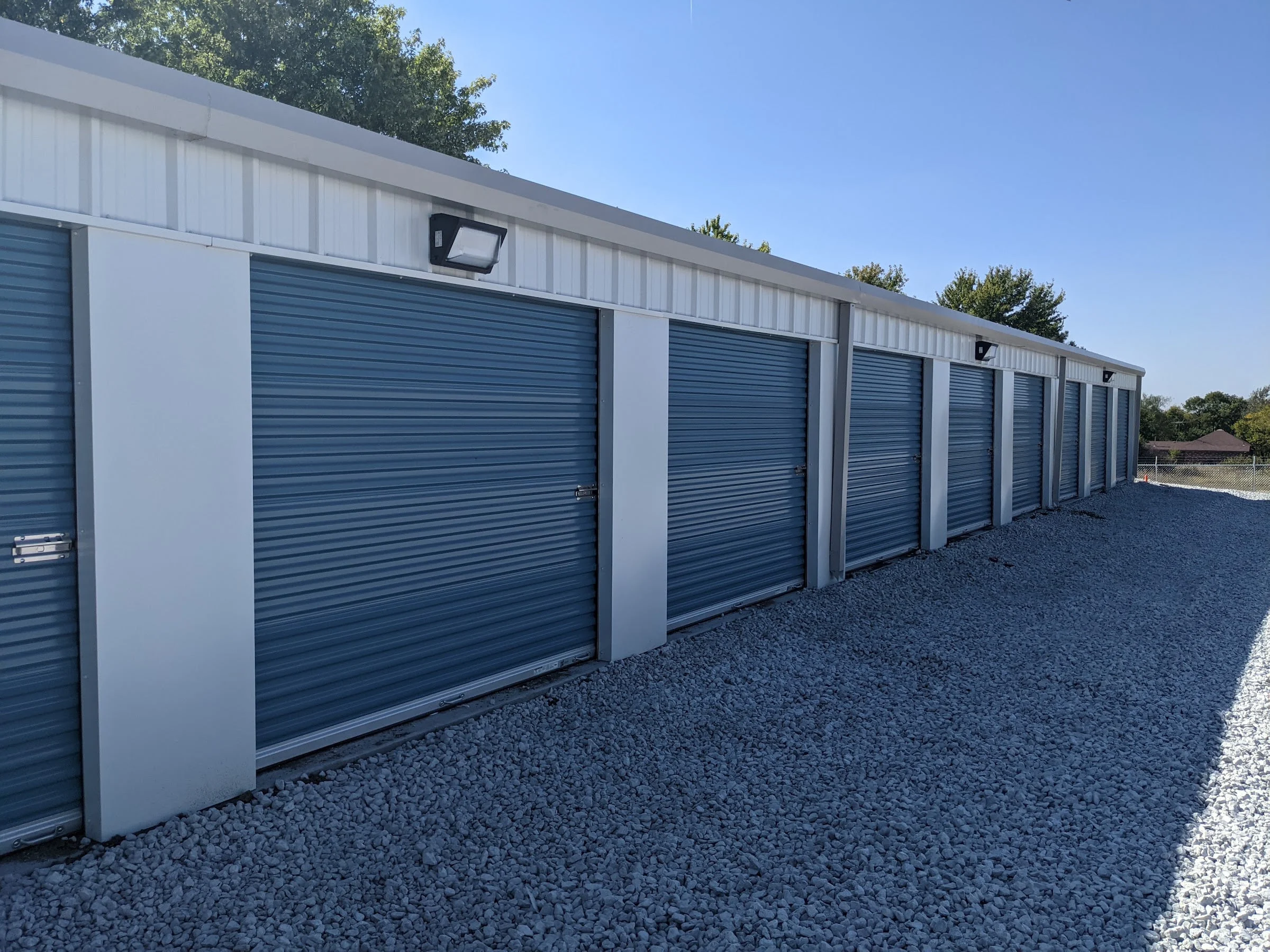 Row of finished self-storage units with blue roll-up doors on a gravel drive
