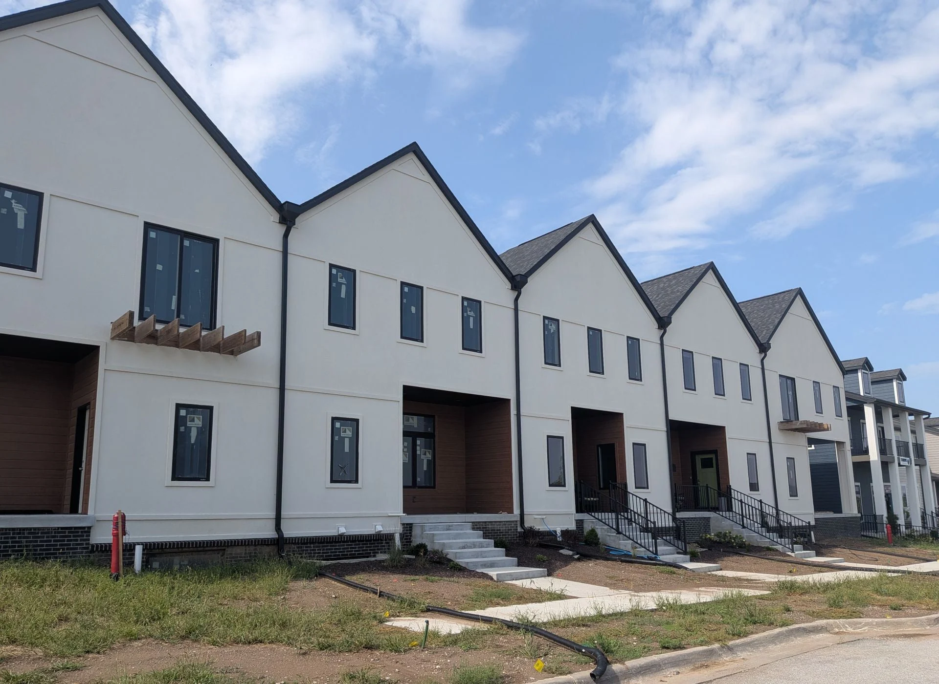 Five white stucco townhome units with gabled roofs and brick bases, nearing completion