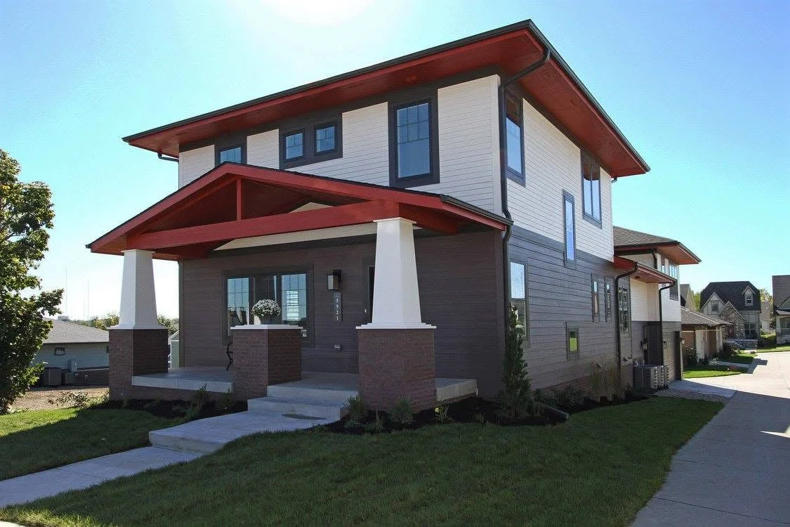Two-story home with deep red roof trim, square porch columns, and a covered front porch