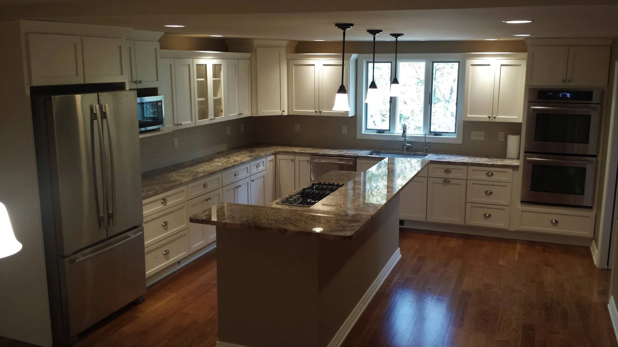 Kitchen in a new addition with white cabinets, granite counters, a cooktop island, and hardwood floors