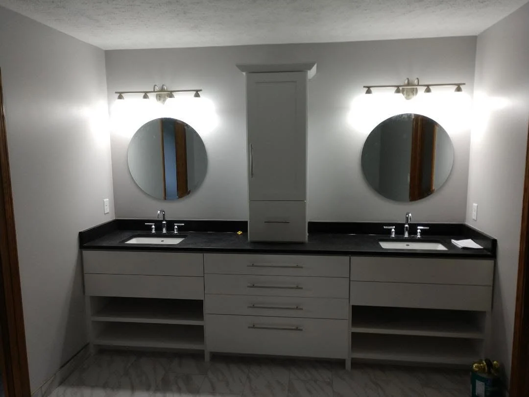 Remodeled bathroom with a double vanity, black countertop, and round mirrors