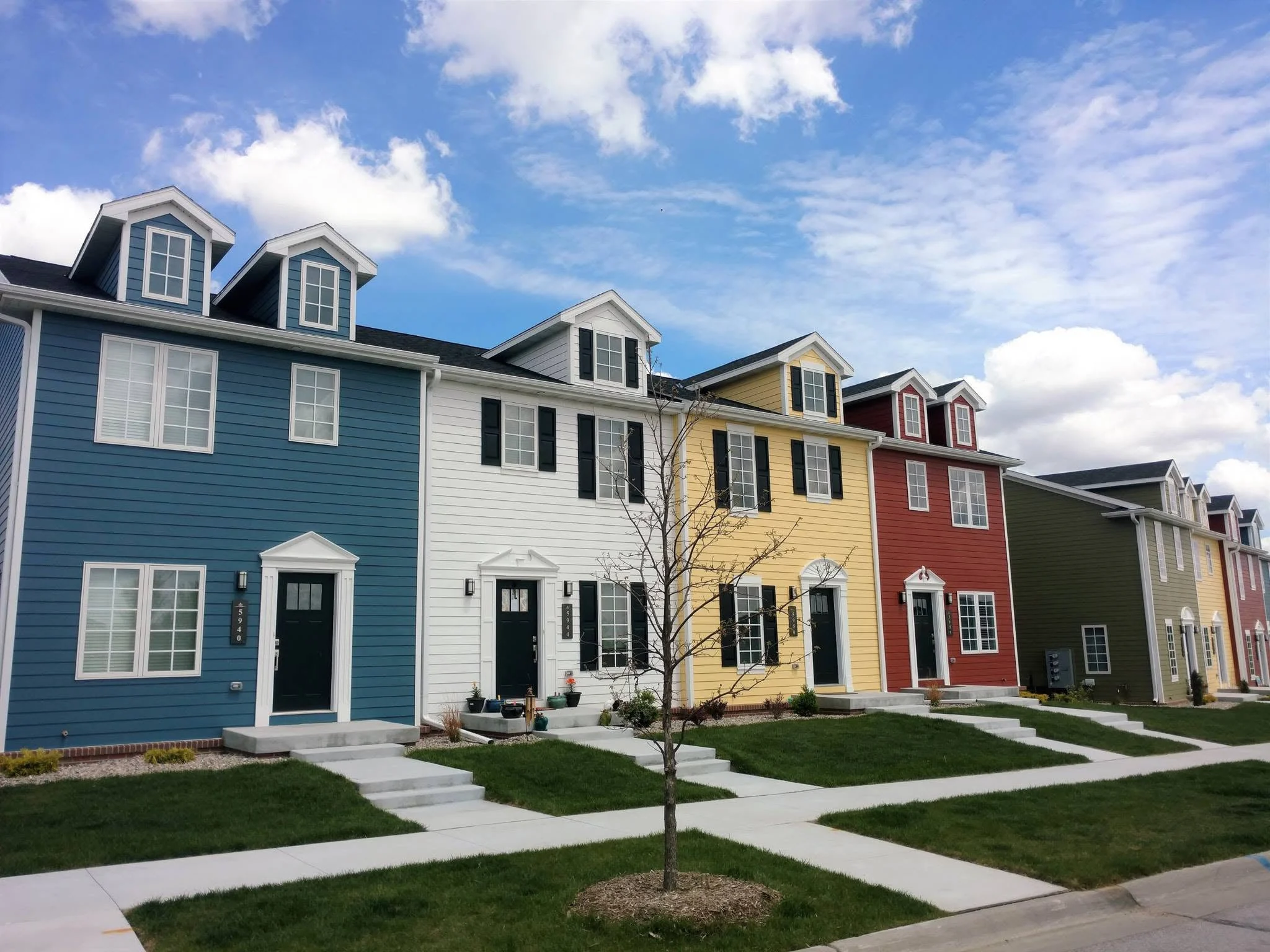 Row of four-plex rental buildings in blue, white, yellow, and red with front porches