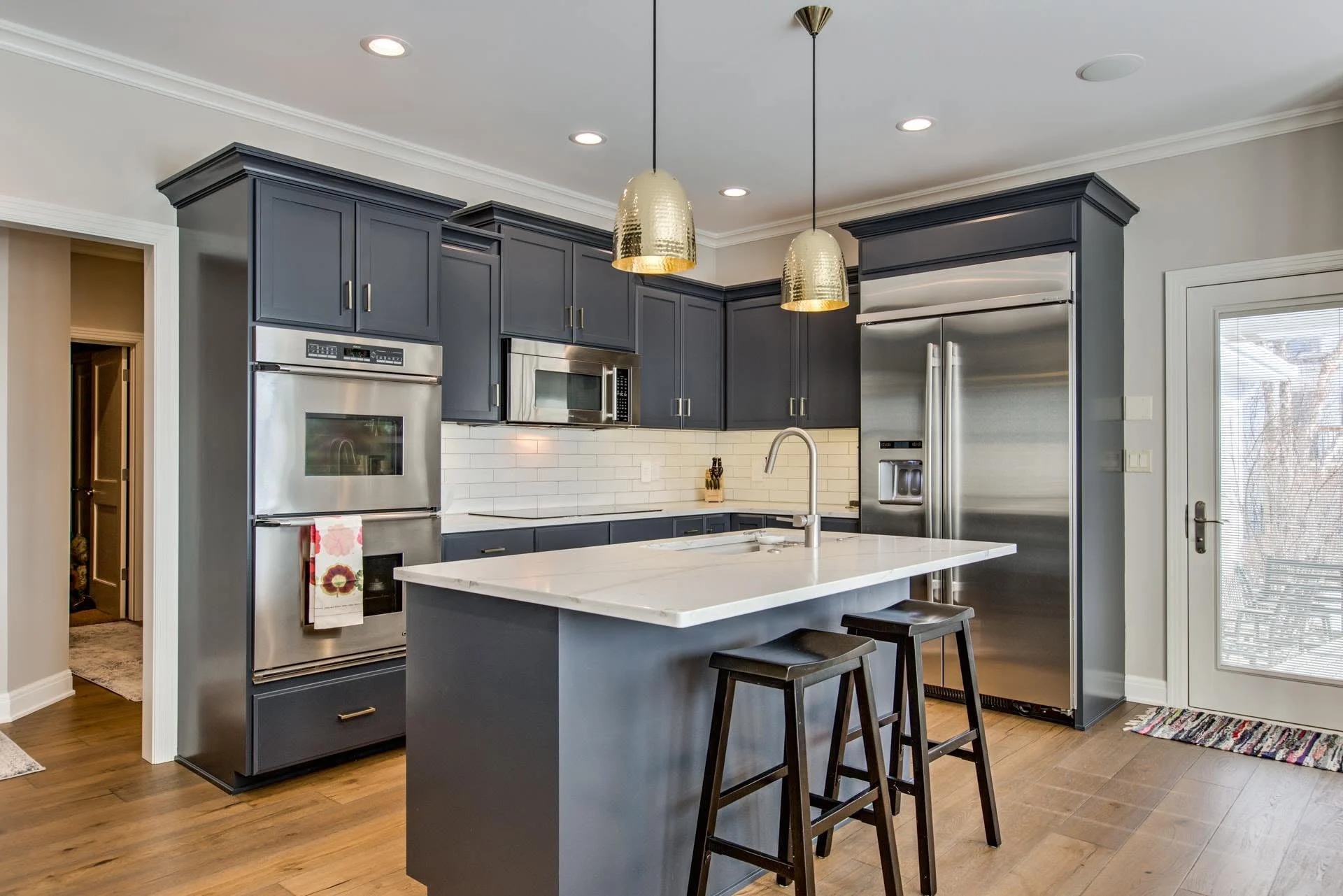 Kitchen with a navy island, white quartz countertops, brass pendants, and double wall ovens