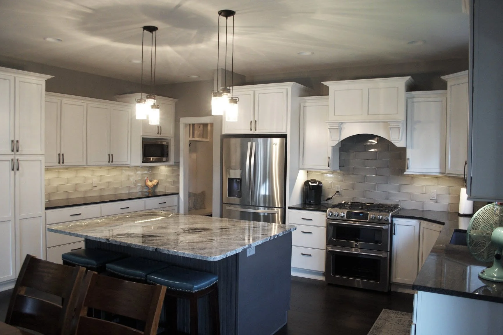 White kitchen with a gray island, glass pendant lights, and a range hood